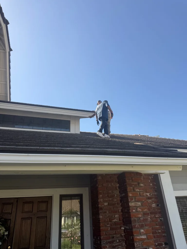 Solar installation crew members walking across dark tile roof with clear blue sky