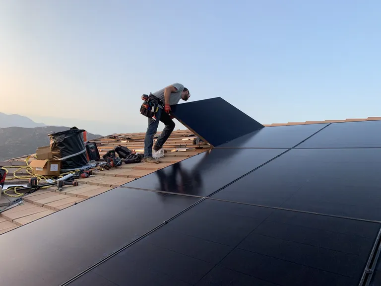 Solar installer placing a panel on a residential roof during golden hour in Devore, CA